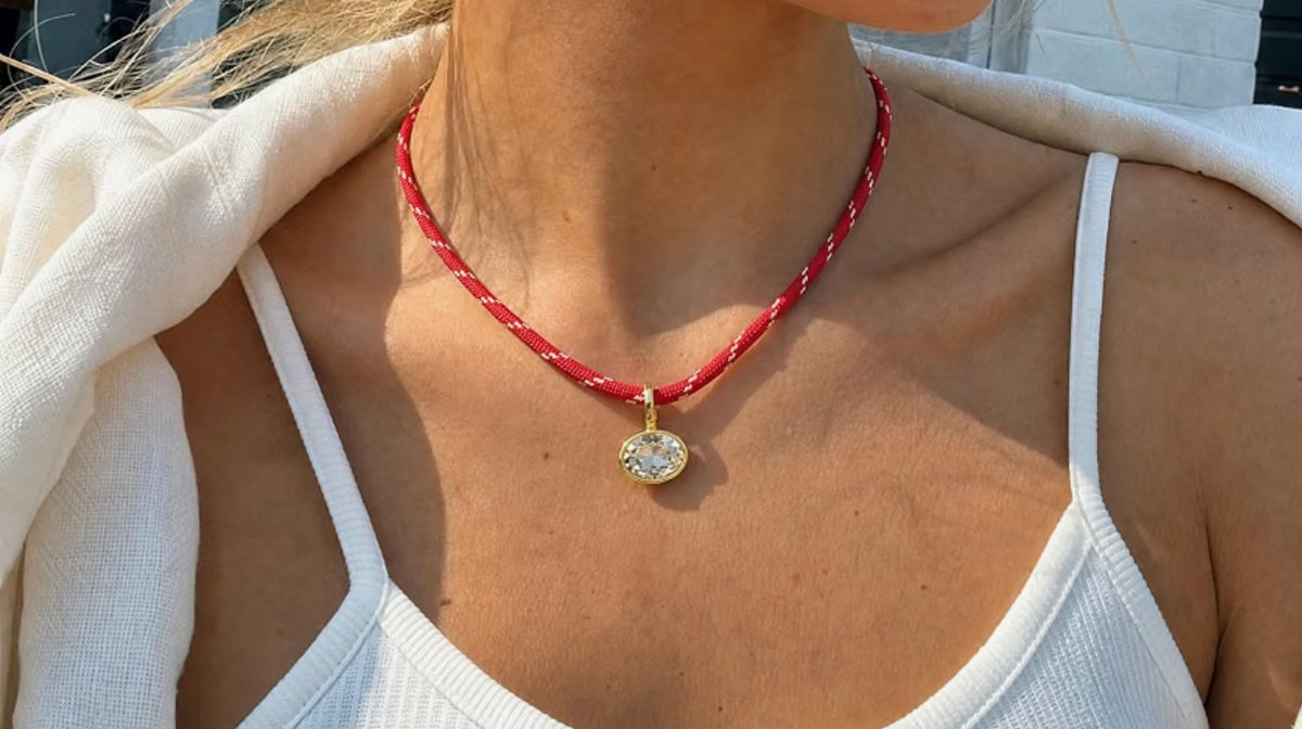 Brilliant oval clear crystal in a gold-tone bezel setting on a patterned red woven paracord.